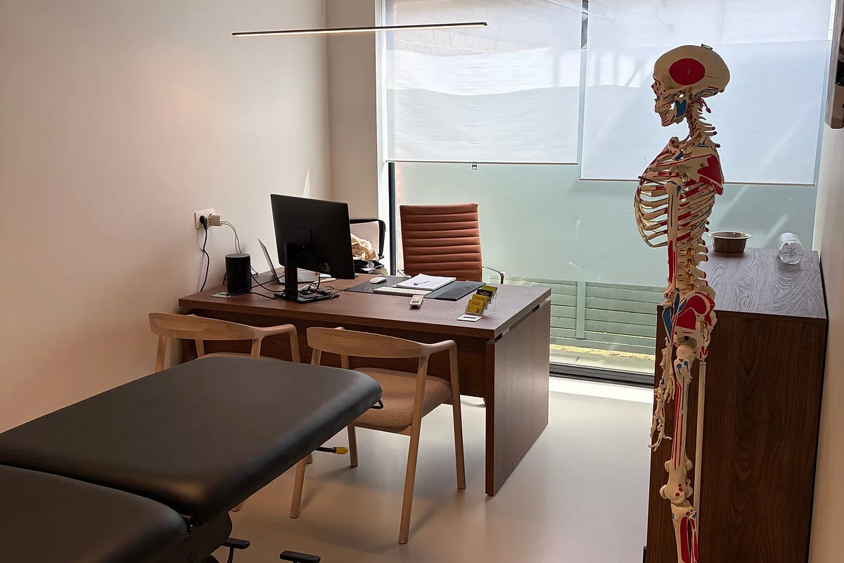 Consultatieruimte met bureau, stoelen en een anatomisch skeletmodel